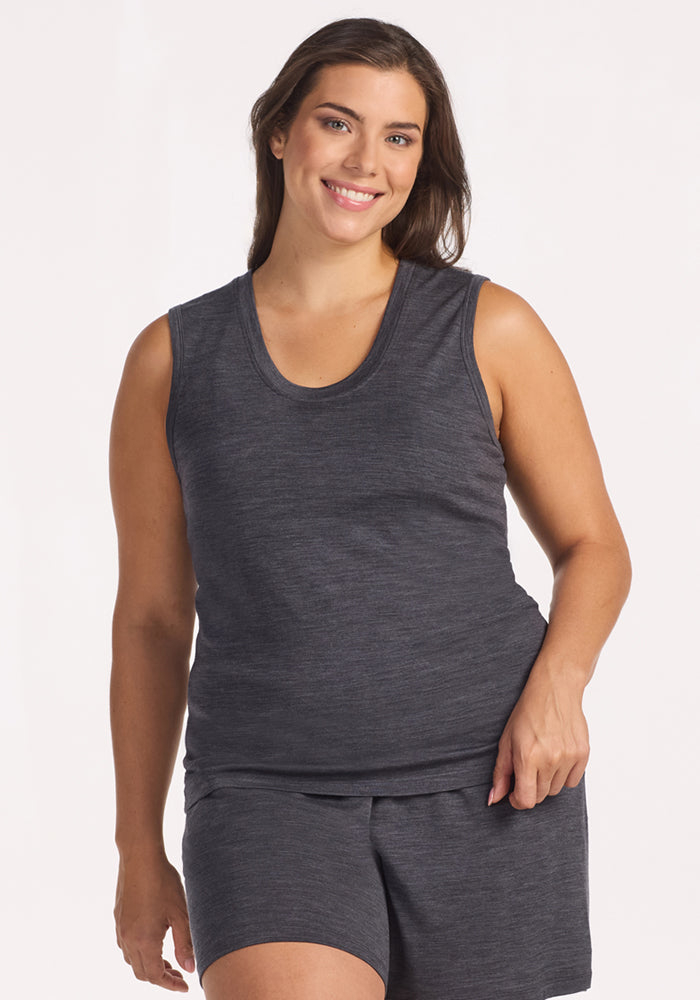 A woman with long brown hair wears the Woolx Phoebe Lounge Tank in Cinder Melange, smiling against a plain light background and highlighting the cooling comfort and lightweight feel of this merino wool sleepwear.