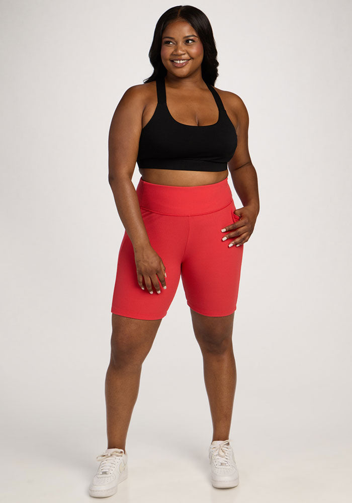 Woman in Woolx Miley Bike Shorts - Hibiscus stands smiling, hand on hip, against a plain background.