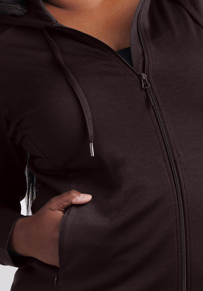 A person wearing the Woolx Ryann Hoodie in French Roast with one hand partially in the pocket, front and drawstrings visible. The background is plain and light.