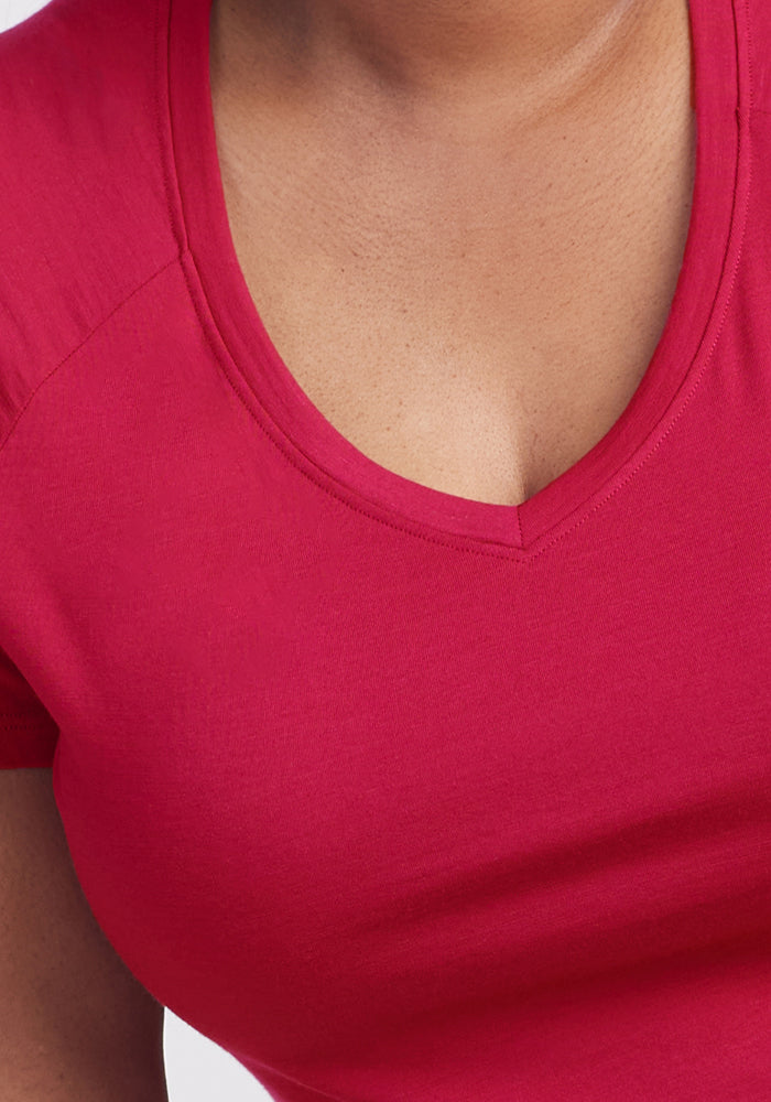 Close-up of a person wearing the Woolx Mia V Neck in Poppy Spark, a bright pink women's moisture-wicking shirt. Only the neck, upper chest, and part of the arm are visible; the face isn't shown.