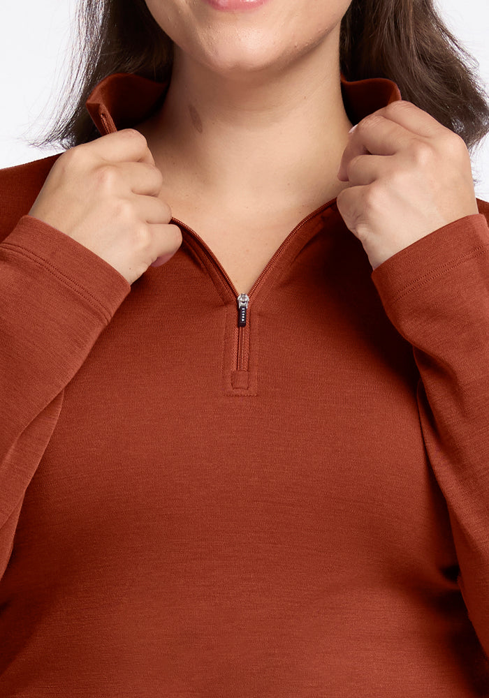 A person wearing the Woolx Brooke 1/4 Zip in Maple Leaf, holding both sides of the collar close to their chin. Only the lower face and upper torso are visible.