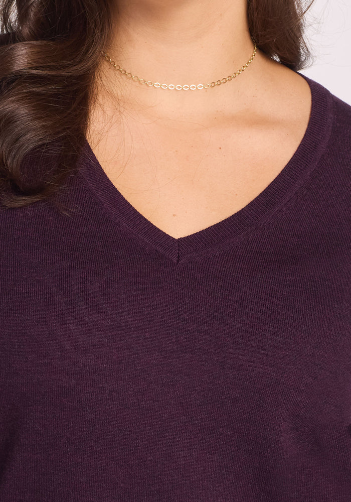 A close-up shows a person wearing the Woolx Francesca Sweater in Deep Plum with a delicate gold chain necklace, highlighting only the lower face, neck, and collarbone.