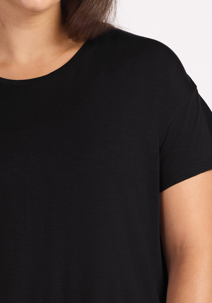 A close-up of a person wearing the Woolx Billie Lounge Tee in black; only the lower half of their face, neck, and upper torso are shown against a white background.
