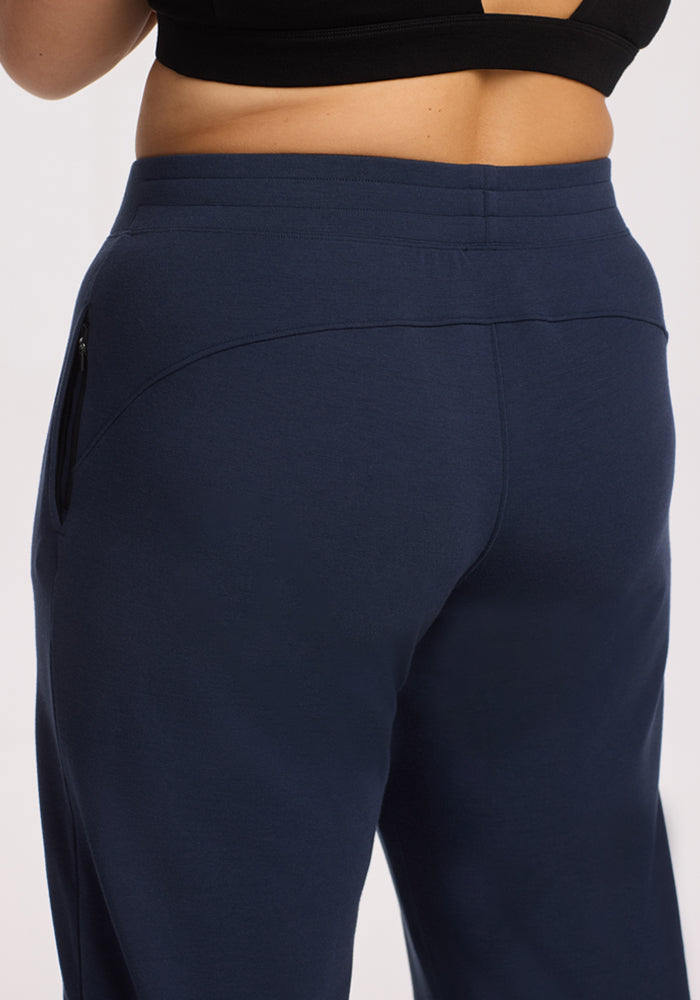 A person is shown from the back and waist down wearing a black sports bra and Woolx Brynn Pants in Deep Navy, highlighting the fit and merino wool fabric of the pants.