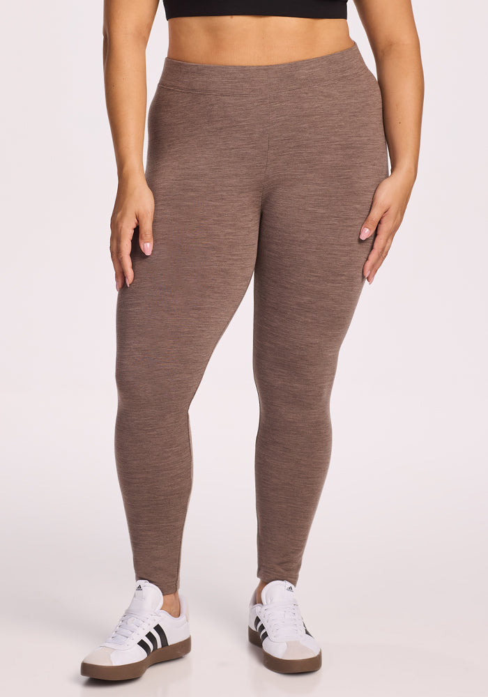 Wearing Woolx Stella Leggings in Simply Taupe, a person stands against a plain light background, facing the camera with hands relaxed by their sides. 