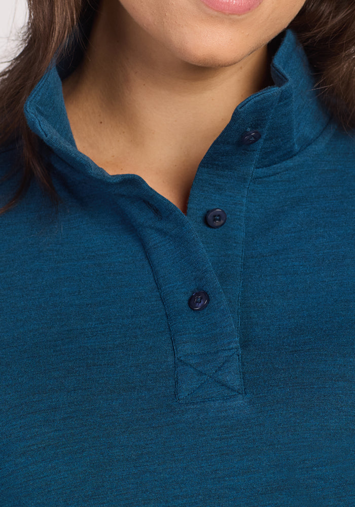 A close-up of a woman wearing the Woolx Annie 3 Button Pullover in Majolica Blue, featuring a stand-up collar, three dark buttons, and visible stitching; only her lower face and neck are shown.