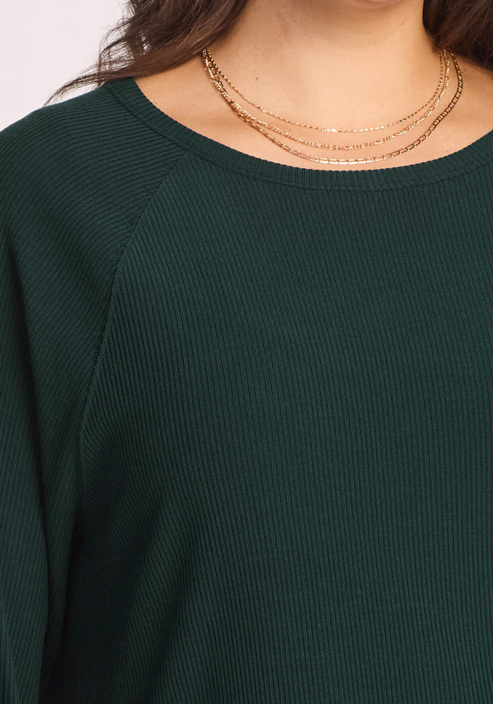 Close-up of a person wearing the Woolx Ainsley Sweater in Deep Timber—this women’s ribbed, temperature-regulating Merino wool layer epitomizes comfort and style, paired with layered gold necklaces. Only the neck, shoulder, and upper chest are visible.