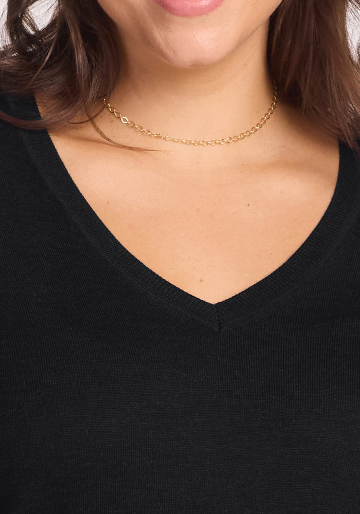 Close-up of a woman wearing a delicate gold chain choker and the Francesca Sweater in Black by Woolx, showing only her neck, lower face, and upper chest.