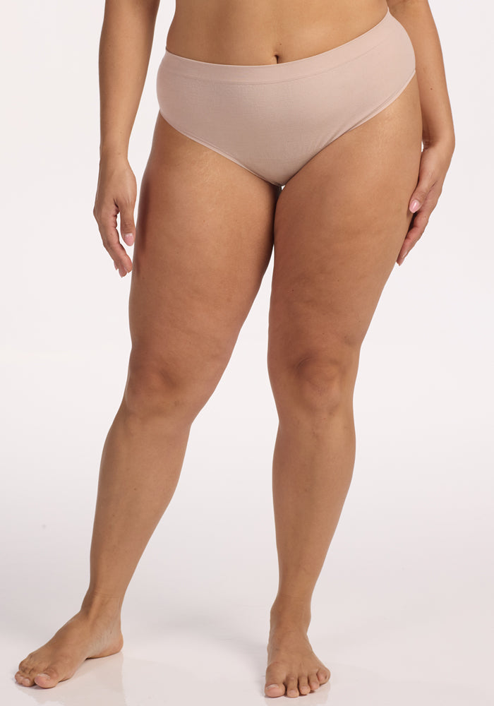 A person stands barefoot against a plain white background, wearing the Woolx Maeve Bikini in Sand. Their arms are relaxed by their sides and their head is out of frame.