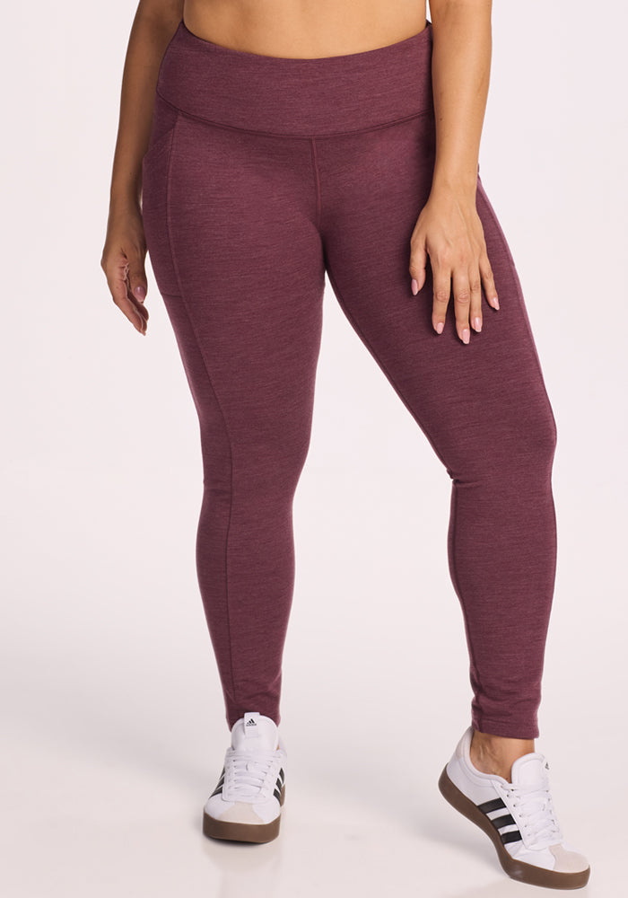 A person models Woolx Frost Duralite® Leggings in Grape Harvest Melange, paired with white sneakers featuring black stripes. Only the lower torso and legs are shown, set against a plain light background. 