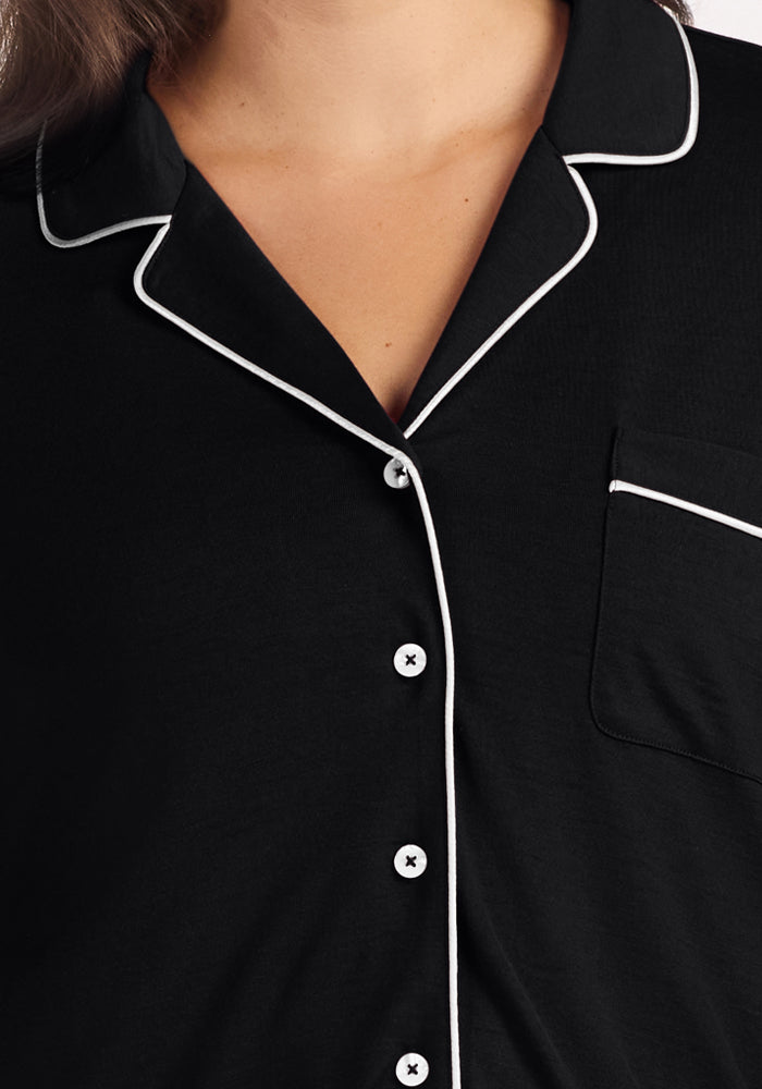 Close-up of a person wearing the Woolx Harper FeatherTouch® Pajama Set in Black, featuring white piping, white buttons, and a left chest pocket—a stylish and comfortable choice for travel.