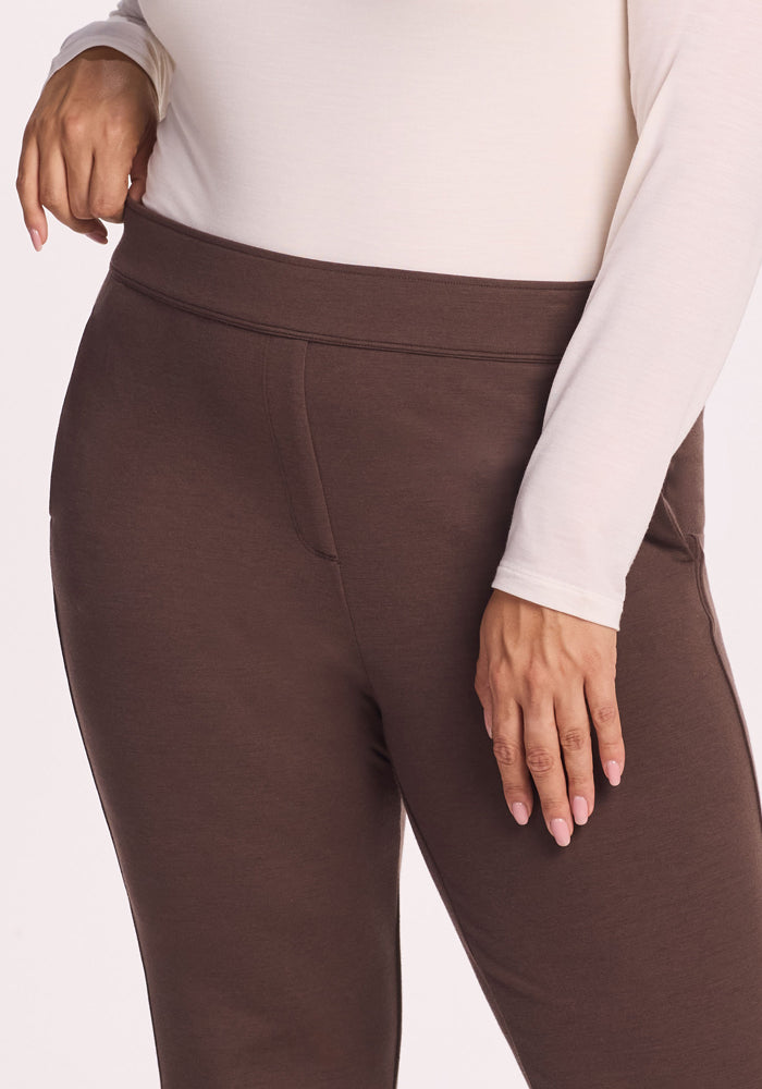 A person models Woolx’s Emerson Straight Leg Pants in Bracken, paired with a long-sleeve white top, standing with one hand on their hip; the image is cropped to show only the torso and upper legs.