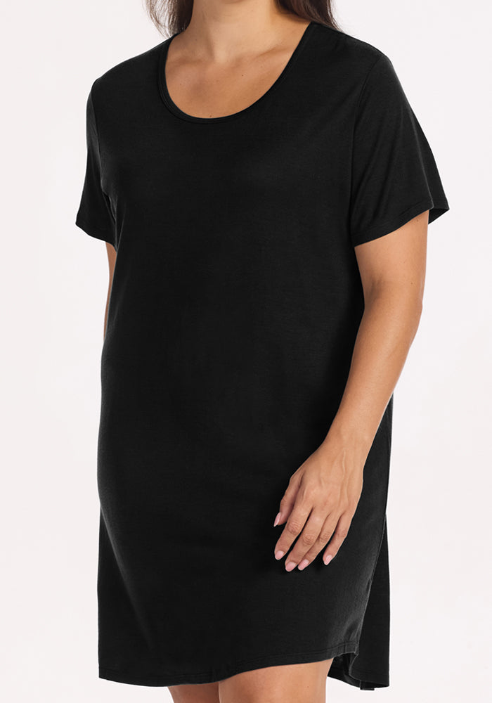 A woman models the Woolx Desi Nightgown in black, a simple temperature-regulating t-shirt dress. She stands against a plain white background, with her head not visible in the image.