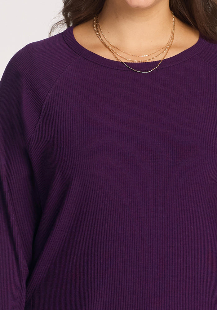 A person wearing the Woolx Ainsley Sweater in Majestic Purple and layered gold necklaces. Only their upper torso and lower half of the face are visible.
