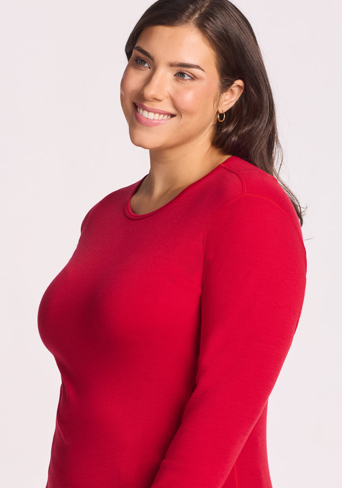 A woman with long dark hair and gold hoop earrings smiles while glancing to the side, wearing the Woolx Hannah Long Sleeve Top in Maraschino Cherry against a plain light background.