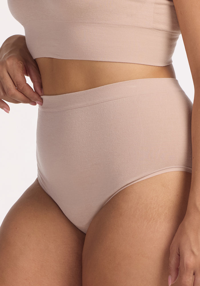 A person wears Woolx Mabel Full Coverage Underwear in Sand, shown from mid-thigh to just below the shoulders against a plain background, emphasizing seamless comfort and modern simplicity.