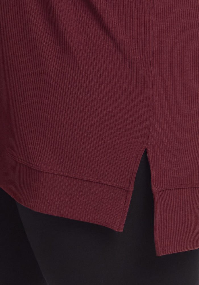 Close-up of the Woolx Evie Ribbed Tunic in Toasted Garnet, featuring a merino wool blend with a small side slit at the hem and black fabric underneath for cozy, temperature-regulating comfort.