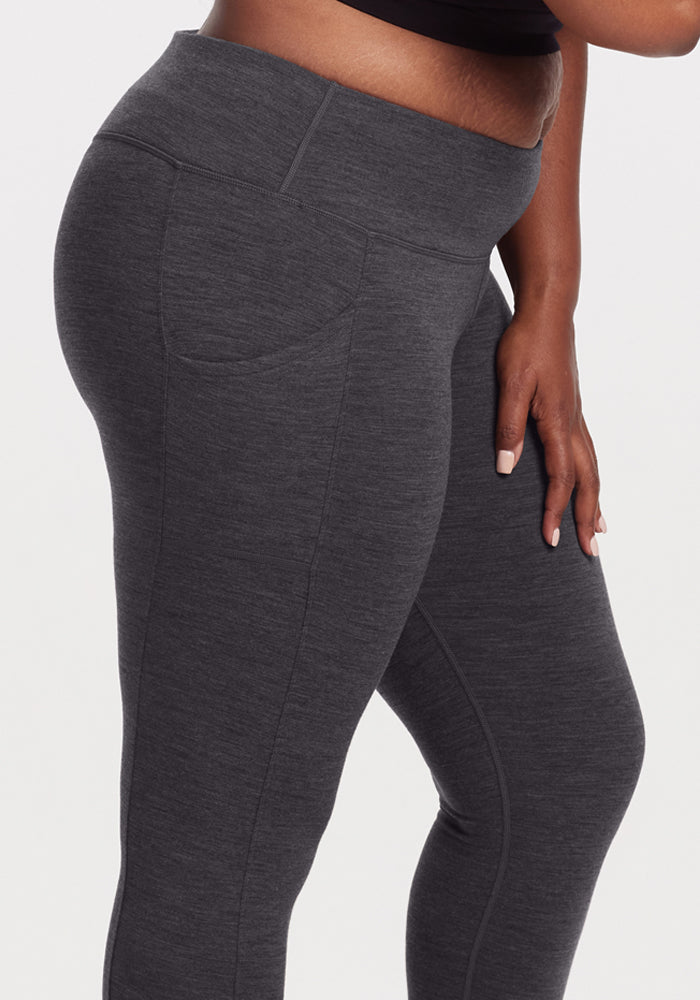 A person wears Woolx Piper Pocket Leggings in Cinder Melange, styled with a black crop top. Shown waist to mid-thigh, they stand against a plain background with one hand resting on their leg.