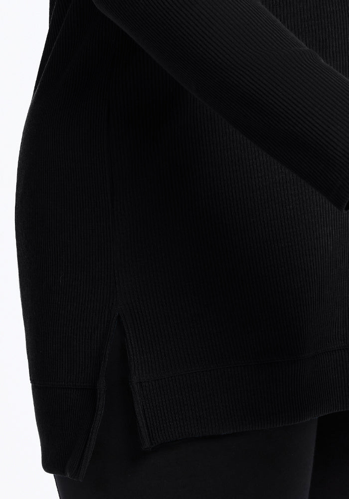 Close-up of the Woolx Evie Petite Tunic in black, featuring a side slit hem, styled with matching black pants.