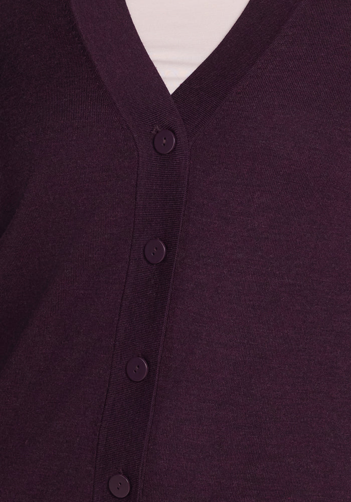 Close-up of the Woolx Gia Sweater in Deep Plum, a Merino wool V-neck cardigan with five matching buttons, worn over a white top. Soft, slightly textured fabric is naturally odor-resistant.