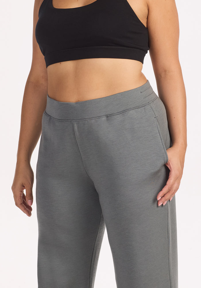 A person wears a black sports bra and Woolx Bree Lounge Pants in Sedona Sage, posing with one hand in a pocket for a relaxed, casual look. The photo, cropped from shoulders to thighs, highlights the comfort of these women’s lounge pants.