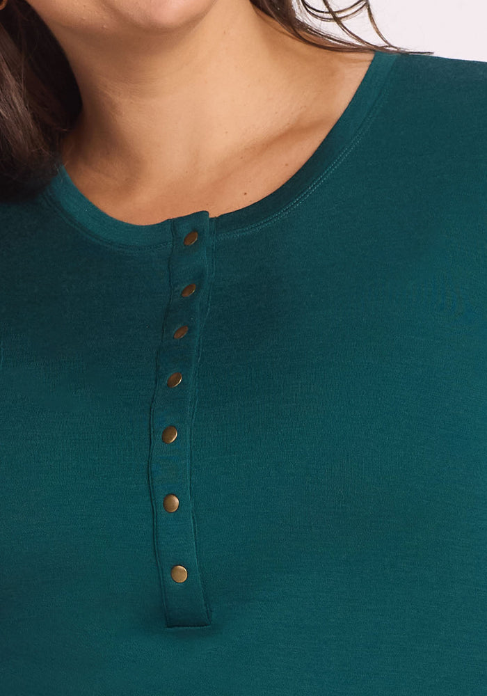 Close-up of a person wearing the Woolx Charlotte Puff Sleeve Top in Riverbank Green, showing only the neck, shoulder, and upper chest. The Merino wool top features a round neckline and Henley-style gold buttons.