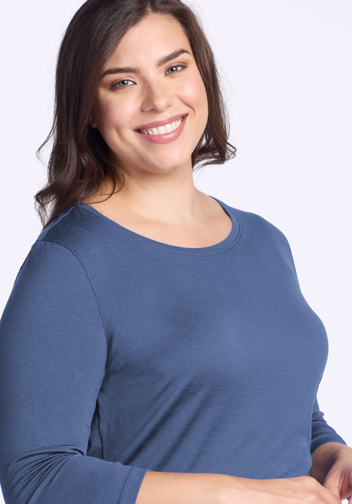 A woman with long brown hair and light skin smiles at the camera, wearing the Woolx Jenny 3/4 Sleeve Crew Neck in Skyline, styled with natural makeup against a plain light background.