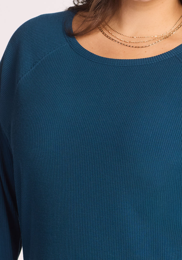 Close-up of a person wearing the Woolx Ainsley Sweater in Majolica Blue, styled with layered gold necklaces. Only the neck, shoulder, and upper chest are visible against a plain light background, highlighting this chic temperature-regulating look.