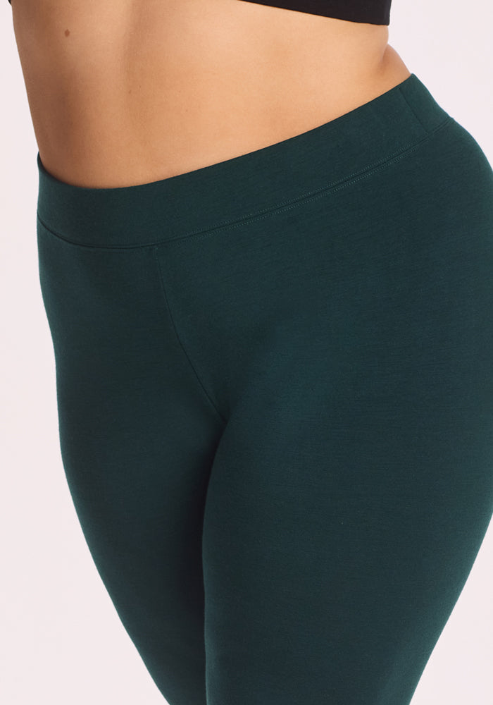 A close-up of a person wearing Woolx Stella Tall - Deep Timber high-waisted leggings and a black crop top, highlighting the waist and upper thigh against a light background.