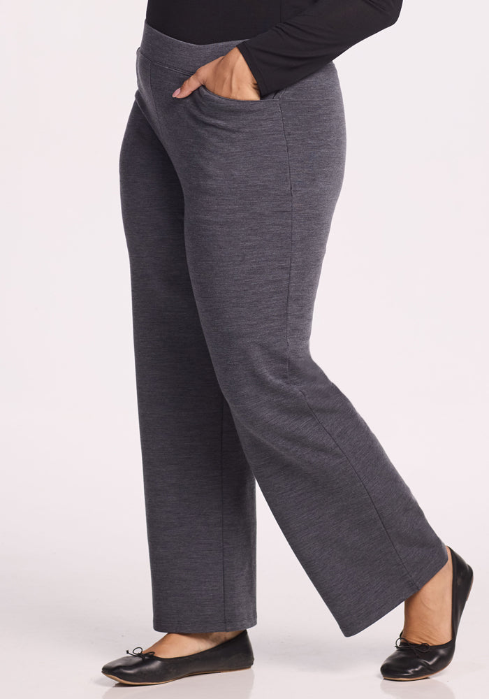 A person wearing Woolx Ellie Wide Leg Pants in Cinder Melange and black ballet flats stands with one hand in their pocket against a plain light background.