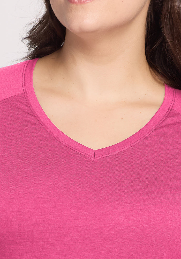 A close-up of a woman wearing the Woolx Mia V Neck in Raspberry Fizz, an odor-resistant Merino wool t-shirt. Only the lower half of her face, neck, and upper chest are visible, with dark hair draped over one shoulder.