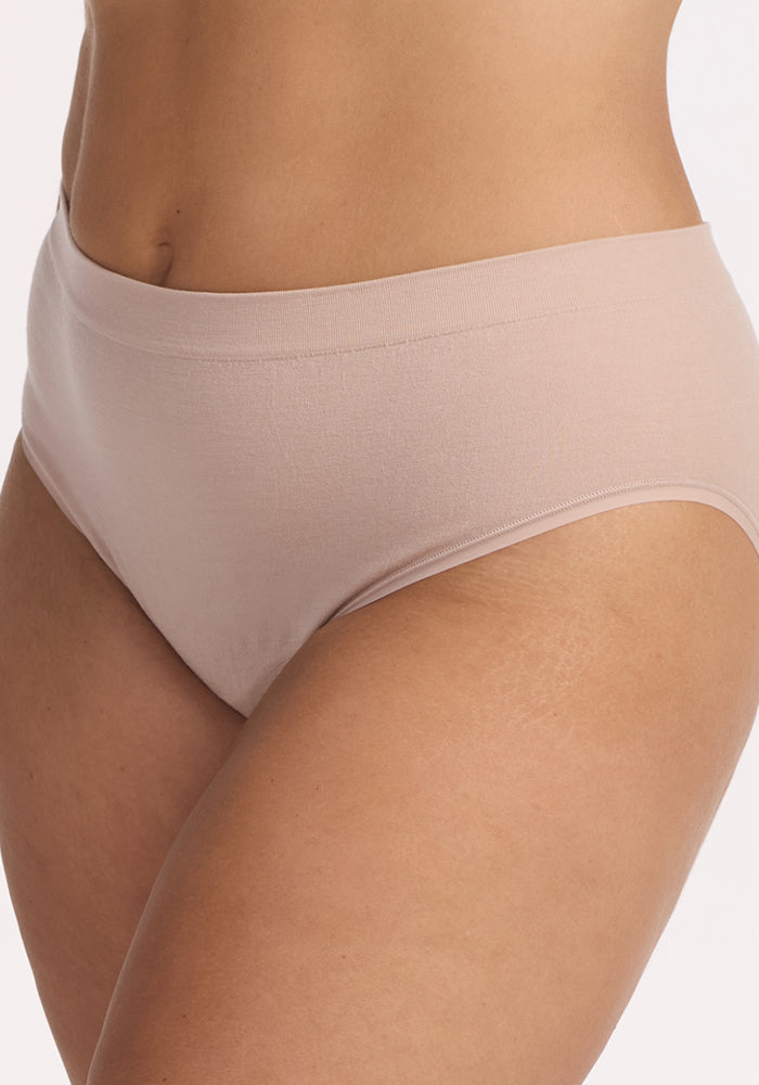 A close-up of a person wearing the Woolx Maeve Bikini in Sand, high-waisted moisture-wicking underwear, showcasing their waist, hips, and upper thighs against a plain light background.