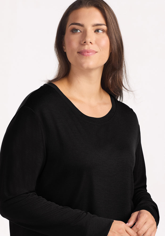 A woman with long brown hair wears the Woolx Ashlie Lounge Top in black and looks slightly upward with a gentle smile, against a plain light background.