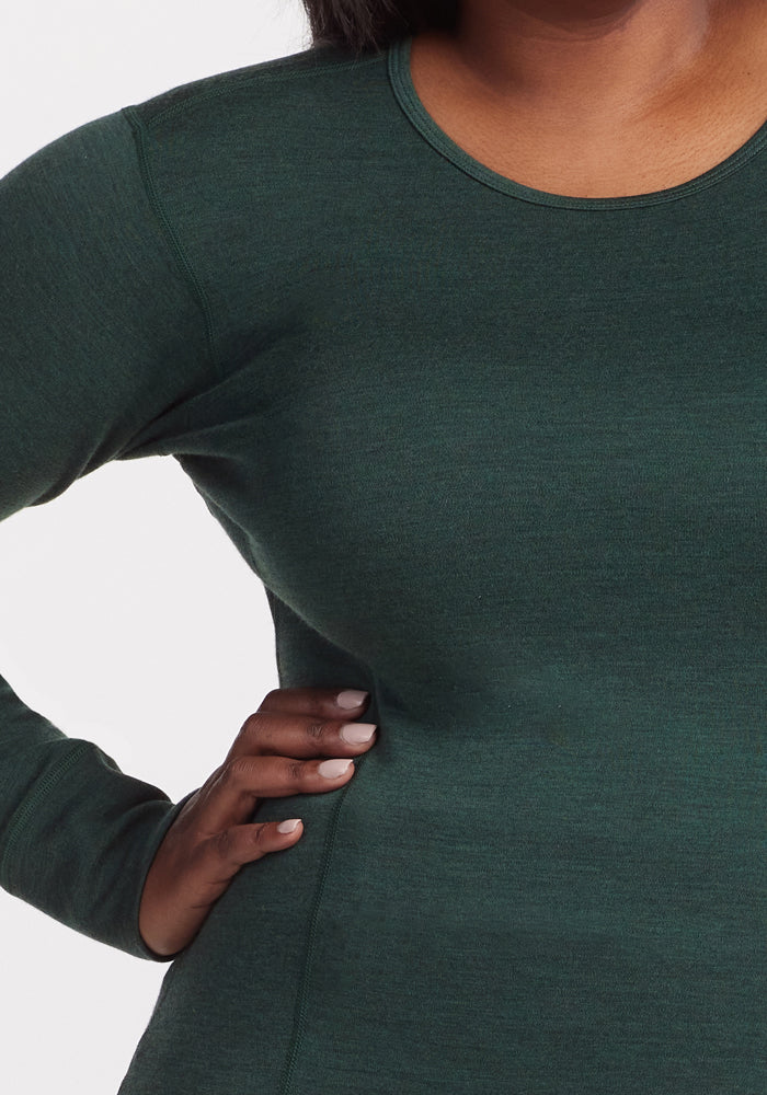 A person models the Woolx Hannah Long Sleeve Top in Forest, showing the torso, arm, and part of the face with one hand on their hip against a white background.