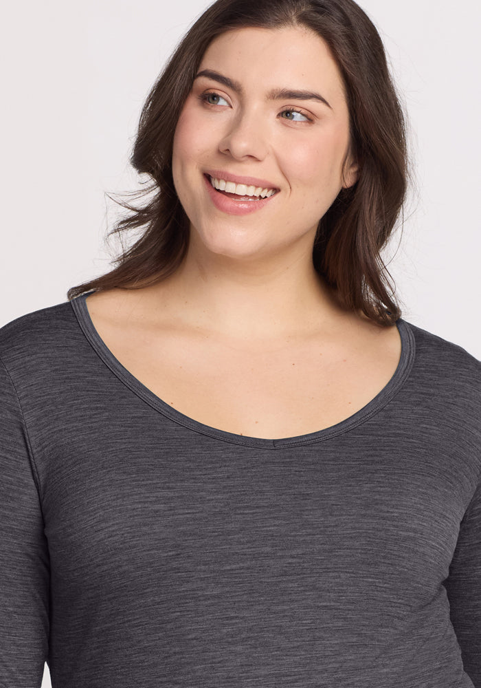 A woman with long brown hair smiles and looks slightly to the side, modeling the Woolx Layla V Neck Top in Cinder Melange against a plain light background.