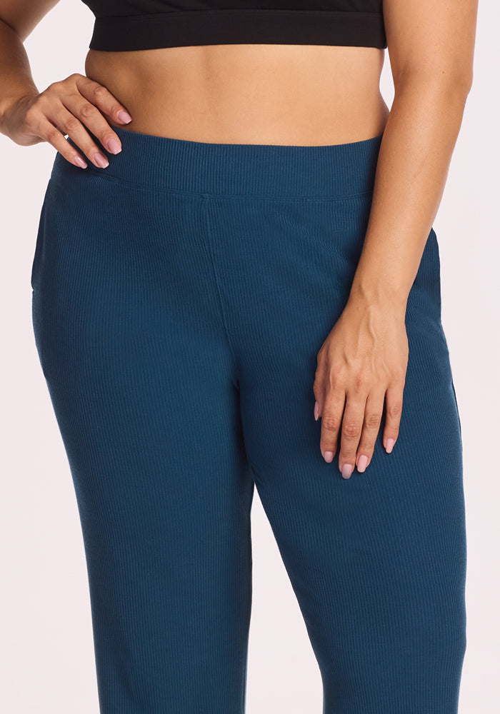 A person wears the Woolx Luca Ribbed Pants in Majolica Blue with a black crop top, one hand on their hip and the other on their thigh, highlighting the comfortable wide-leg fit.