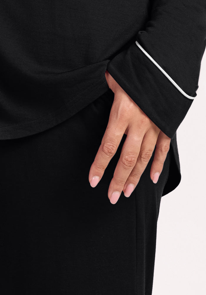 A close-up of a hand resting by their side, wearing the Woolx Harper FeatherTouch® Pajama Set in black with a white-piped sleeve, set against a light background.