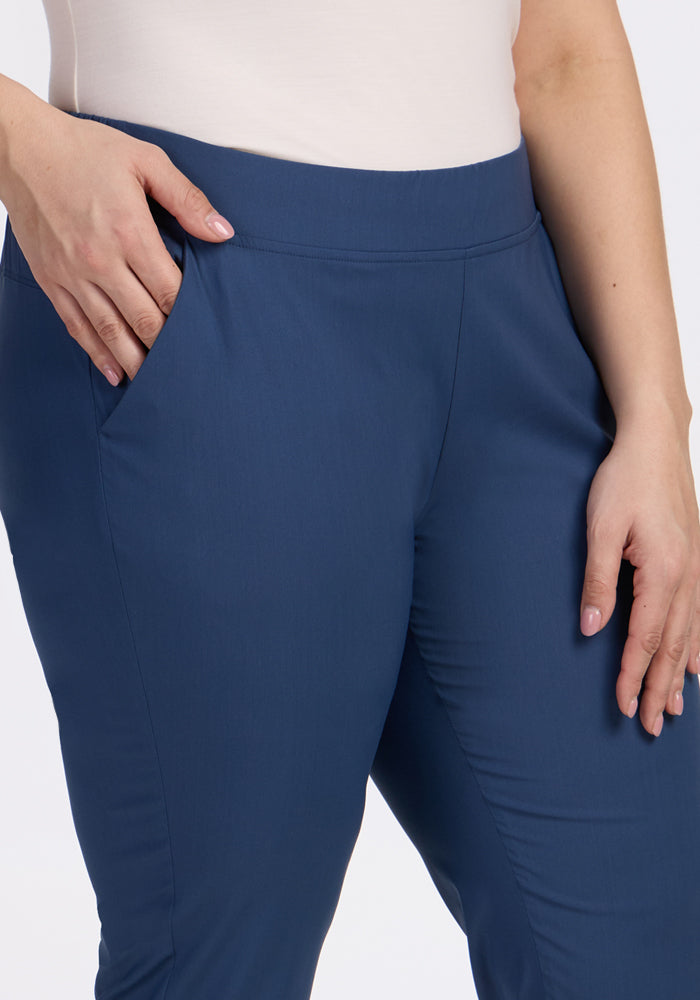 A person wears Woolx Nicole Ankle Pants in Vintage Indigo with a light top, shown from waist to mid-thigh, one hand in pocket and the other resting by their side.