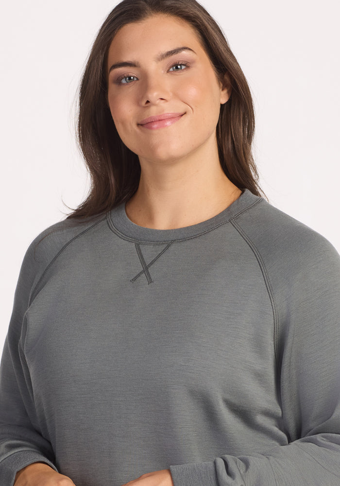 A woman with long brown hair wears the Woolx Bailey Crewneck Sweatshirt in Sedona Sage, smiling softly at the camera against a plain light background.