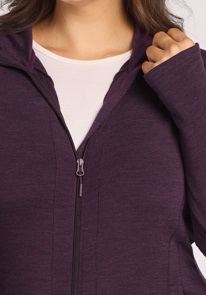 A person wearing a Woolx Zoey Zip Up Hoodie in Deep Plum over a white shirt, shown from shoulders to mid-chest, holds the hoodie near the collar with one hand.