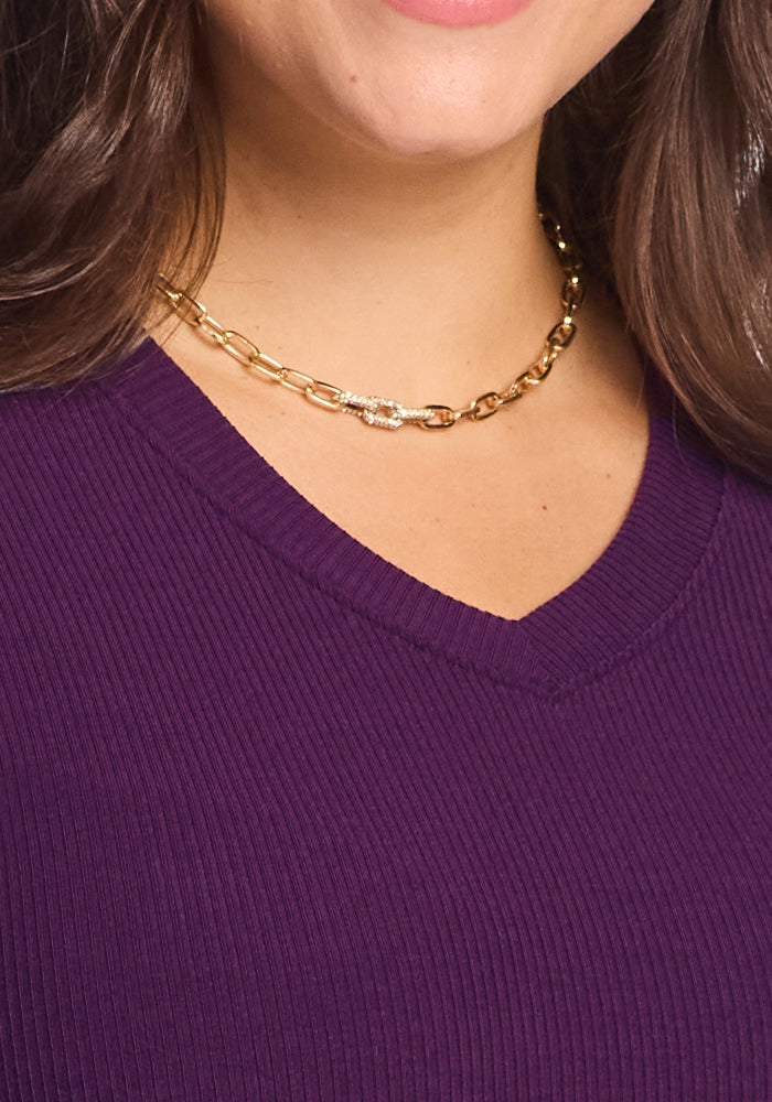 A woman wears a gold chain necklace and the Woolx Evie Ribbed Tunic in Majestic Purple. Only the lower half of her face, neck, and upper chest are visible.