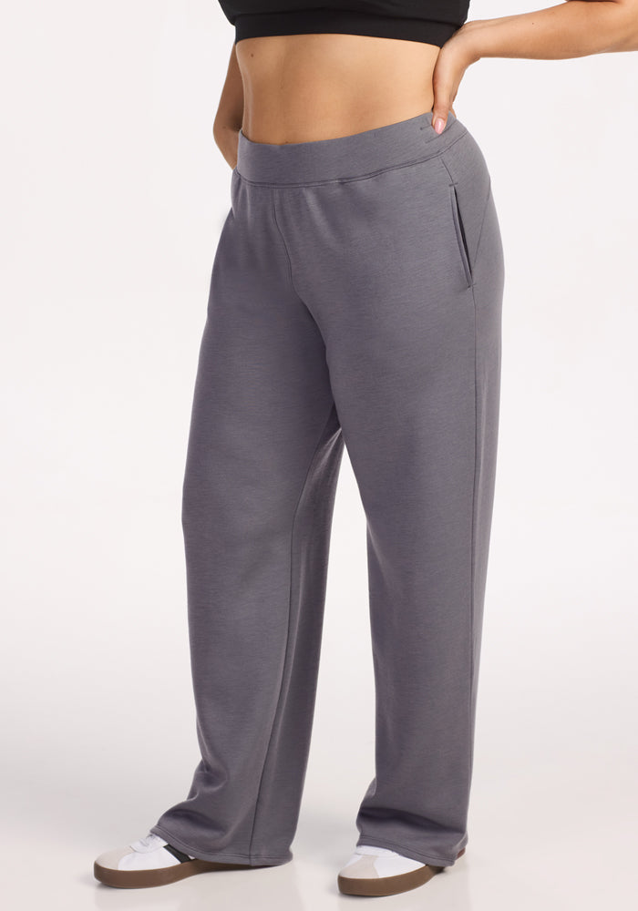 A person stands with one hand on their hip, wearing Woolx Bree Lounge Pants in Arctic Dusk. The gray, relaxed fit pants feature side pockets and a high, wide waistband. The photo is cropped from the shoulders down and shows white sneakers.