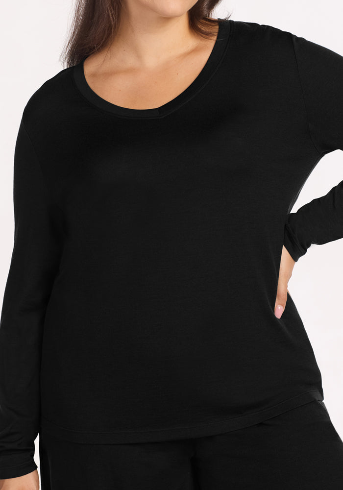 A woman wears the Woolx Lily V Neck Lounge Top in black with black pants, standing with one hand on her hip against a plain white background. Her head is partially out of frame.