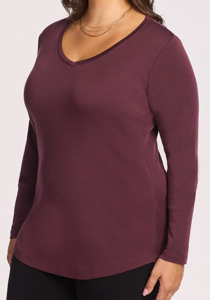 A woman is shown from shoulders to hips wearing the Woolx Eva Tunic in Chocolate Fig—a long-sleeved Merino wool V-neck—paired with layered gold necklaces.