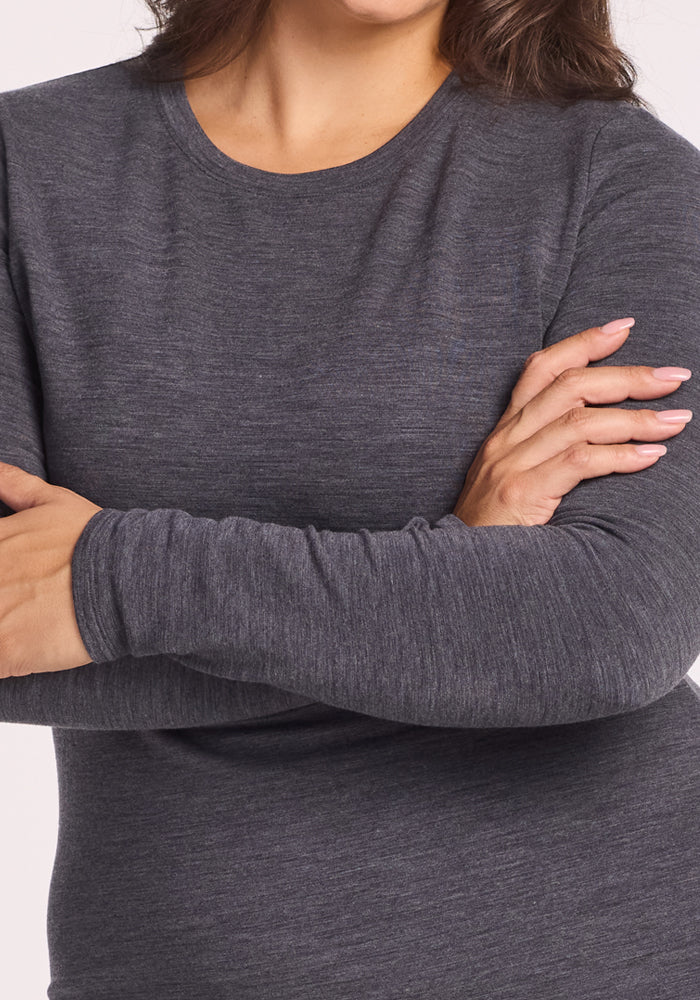 A woman stands with her arms crossed, showing only her torso and lower face, wearing the Woolx Sadie Baselayer Top in Cinder Melange. Her nails are manicured in a pale pink shade.