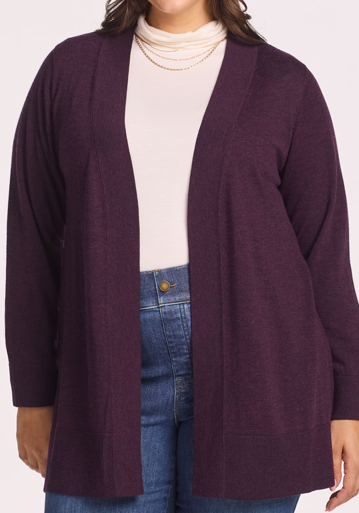 A person wearing the Woolx Macie Sweater in Deep Plum over a white turtleneck, paired with layered gold necklaces and blue high-waisted jeans.