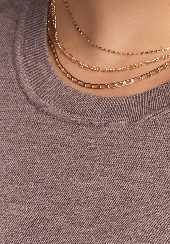 Close-up of a person wearing the Woolx Anna Crew Sweater in Simply Taupe, styled with layered gold chain necklaces.