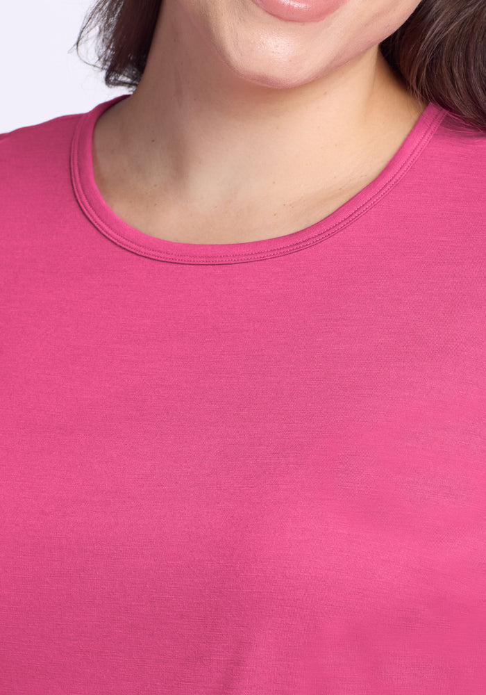 A close-up of a person wearing the Woolx Liza Crew Neck Tee in Raspberry Fizz, showing part of their face, neck, and shoulder as they smile slightly.