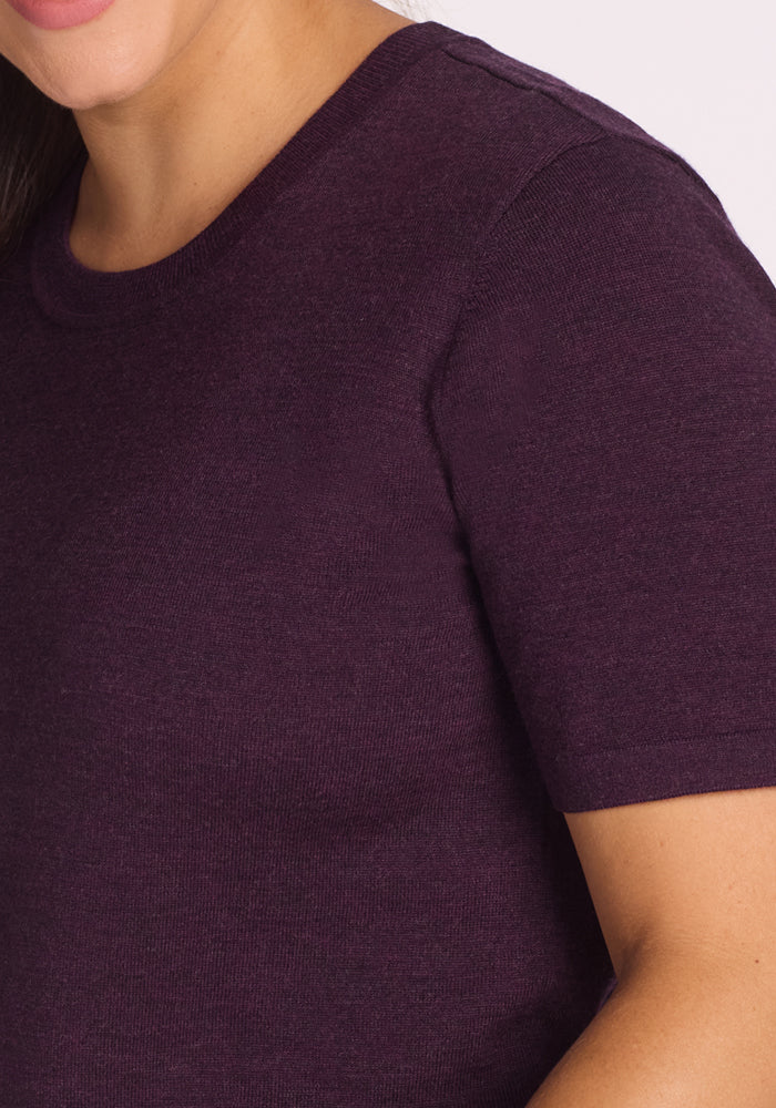 Close-up of a woman wearing the Woolx Anna Crew Sweater in Deep Plum, a short sleeve merino wool top with a classic crew neck; only her lower face, shoulder, and upper arm are visible against a light background.