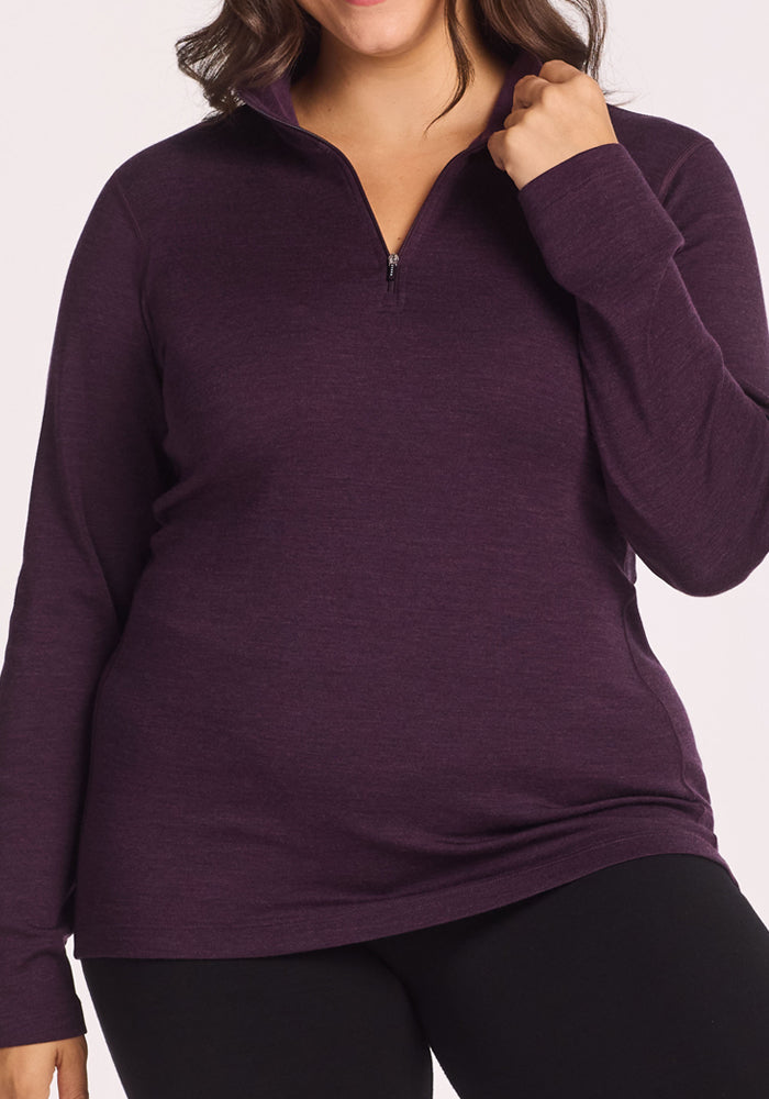 A person wears the Woolx Brooke 1/4 Zip in Deep Plum with black pants, one hand holding the collar and the other at their side. The image is cropped from shoulders to thighs.